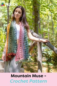 a woman standing on top of a wooden bridge wearing a crochet shawl