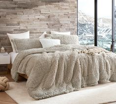 a bedroom with a bed covered in fluffy blankets and pillows next to a large window