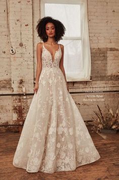 a woman standing in front of a window wearing a wedding dress with flowers on it