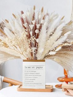 an arrangement of dried flowers in a vase on a table with a sign that says le sac en papiet