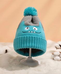 a blue knitted hat with eyes and a pom - pom