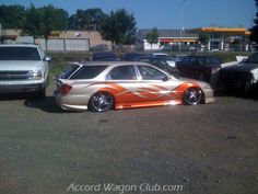 an orange and white car parked in a parking lot next to other cars with flames painted on them