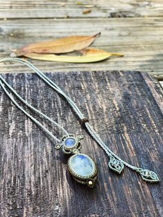 two necklaces sitting on top of a piece of wood next to a brown leaf