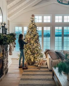 a woman is decorating a christmas tree in the living room with fireplace and windows