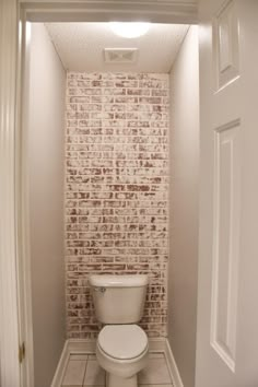 a white toilet sitting inside of a bathroom next to a wall with bricks on it