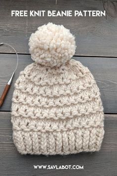 a crocheted hat with a pom - pom sits on top of a wooden