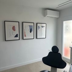 three framed pictures hang on the wall above a black chair in an empty room with white walls