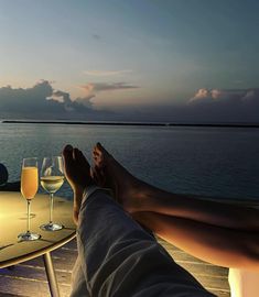 two people sitting at a table with wine glasses on it and one person holding their feet up in the air