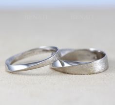 two silver wedding rings sitting on top of a white table next to eachother