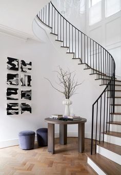 a room with a table, stools and a spiral staircase in the background is an art piece