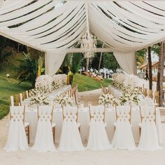 an outdoor wedding setup with white flowers and draping on the ceiling, draped in fabric