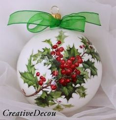 a white ornament with holly and red berries on it, hanging from a green ribbon