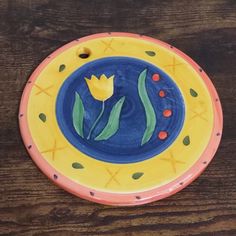 a yellow and blue plate with flowers painted on the side, sitting on a wooden table