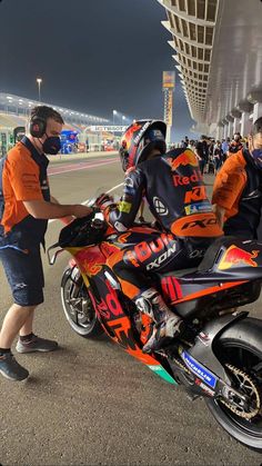 two men in orange and black uniforms are on a red motorcycle while another man is wearing headphones