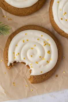 three cookies with white frosting and gold sprinkles on top of brown paper