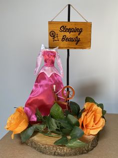 a wooden sign that says sleeping beauty with a pink dress and orange roses around it