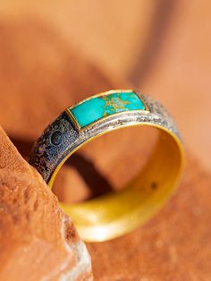 a gold and turquoise ring sitting on top of a piece of wood next to a rock