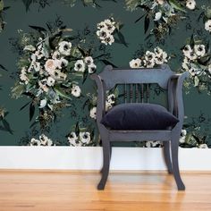 a black chair sitting in front of a wall with white flowers and green leaves on it