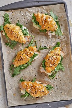 several croissants with greens and sesame seeds on a sheet of wax paper