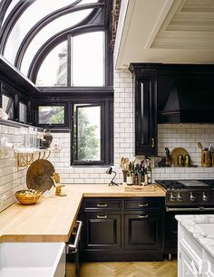 a kitchen with black cabinets and wooden counter tops in front of a large window that has arched windows