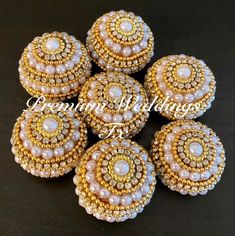 six beaded buttons in gold and white with pearls on the center, sitting on a black surface