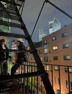 two people standing on top of a metal stair case in front of a cityscape