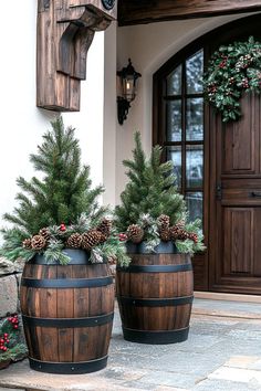 two wooden barrels with pine cones and evergreens in front of a house decorated for christmas