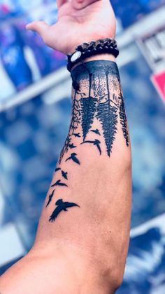 a man's arm with birds flying around it and trees on the wrist tattoo