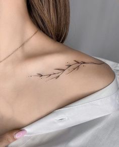 the back of a woman's shoulder with a branch tattoo on it