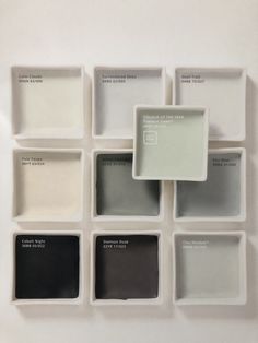 several different shades of gray and white paint arranged in square trays on the wall