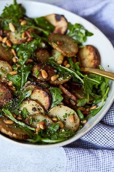 a white bowl filled with spinach, potatoes and toasted almonds on top of a blue table cloth