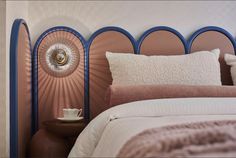 a bed with pink and blue headboard next to a table with a cup on it