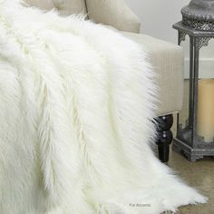 a white fur blanket sitting on top of a couch next to a candle