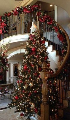 a christmas tree with red and gold ornaments on it in front of a spiral staircase