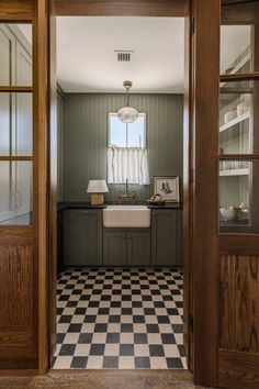 an open door leading to a kitchen with checkered tile flooring and green walls