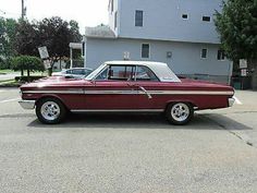 an old red and white car parked in a parking lot next to a large house