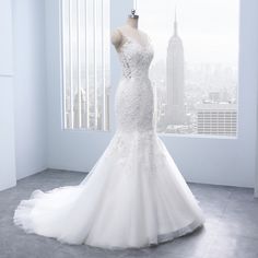 a white wedding dress on display in front of a window with the city skyline behind it