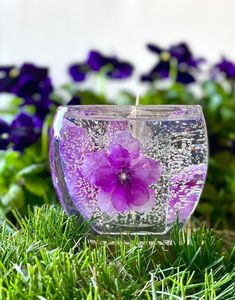 a purple flower floating in a glass bowl filled with water on top of green grass