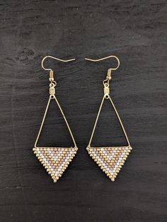 a pair of gold and white earrings on a wooden surface with beads hanging from it