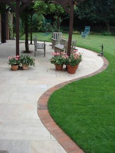 an outdoor patio with potted plants on the side and chairs in the back yard