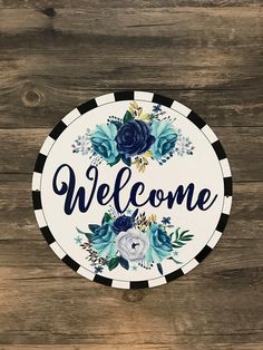 a welcome sign with blue flowers and greenery on the side of a wooden wall