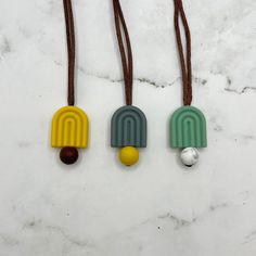 three necklaces with different colors and shapes hanging from brown cords on a marble surface