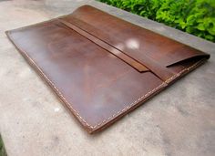 a brown leather ipad case sitting on top of a cement table next to green plants