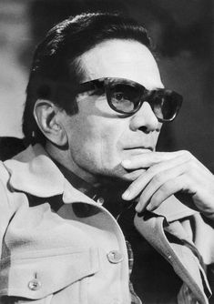 a man in sunglasses sitting down with his hand on his chin and looking off to the side