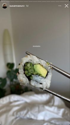 a sushi roll with avocado and cucumber on it is being held up by a pair of tongs