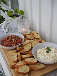 a wooden table topped with bowls of food and bread slices next to a bowl of salsa