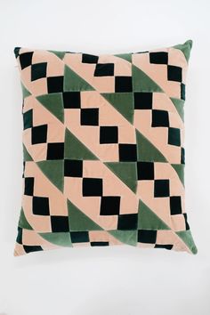 a green, pink and black pillow with squares on it's back cover is sitting against a white wall