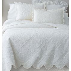 a white bed with ruffled edges and pillows