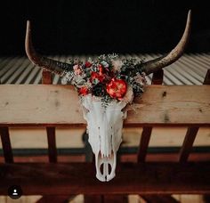 an animal skull with flowers on it's head hanging from a wooden beam in front of a building