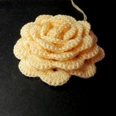 a crocheted yellow rose is shown on a black surface with a metal hook